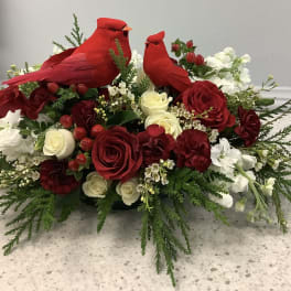 Red cardinal figurines sit in a red and white floral arrangement with roses.