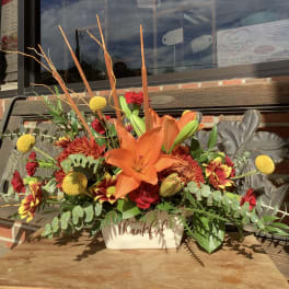 Orange lily and mixed flowers in a cream container