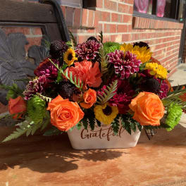 Orange roses and mixed mums in a white ceramic container