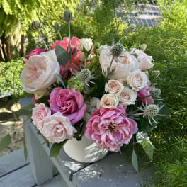 Pink and white roses in a white vase with spiky thistle accents