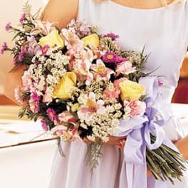 Woman holding a mixed bouquet of pink and yellow flowers with a lavender ribbon