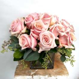 Pink roses arranged in a square glass vase with greenery