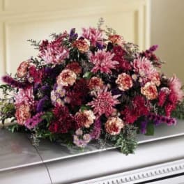 Large pink and purple floral casket spray on a silver casket