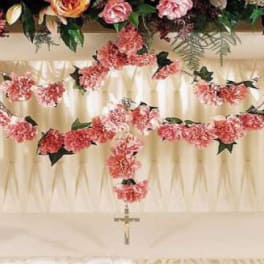 Pink floral garlands draped over a white draped backdrop with a hanging cross
