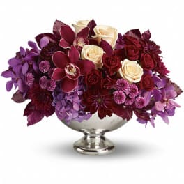 Purple and burgundy floral arrangement in a silver pedestal bowl