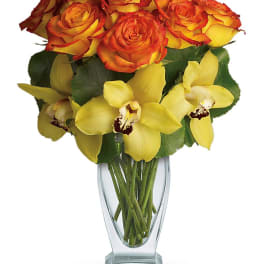 Orange and yellow roses with yellow orchids in a clear glass vase