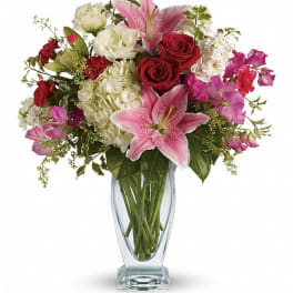 Pink lilies, red roses, and white blooms in a clear glass vase