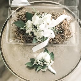 White rose wrist corsage with matching boutonniere on a round table
