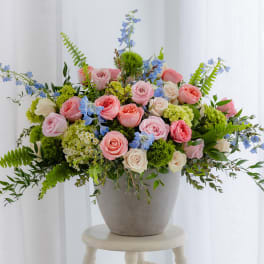 Low gray pot of pink roses, green hydrangeas, and blue delphinium arranged wide on a stool
