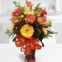 Bouquet of orange roses and yellow gerbera daisies in a vase with a ribbon