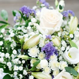 White roses, lilies, and purple filler flowers in a bouquet