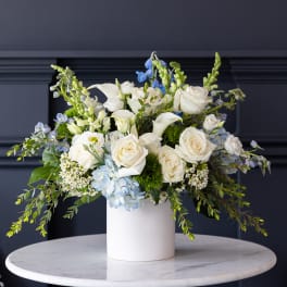 White roses and calla lilies in a white vase with blue accents