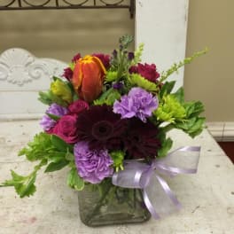 Mixed bouquet in a square glass vase with a lavender ribbon