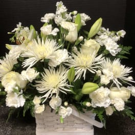 White floral arrangement in a white basket with lilies and spider mums