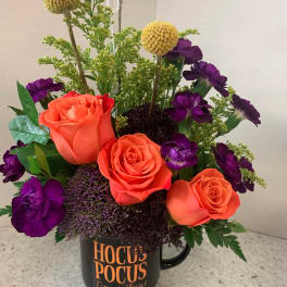 Orange roses and purple flowers arranged in a black mug