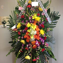 Large standing floral spray with colorful mixed blooms and white ribbons