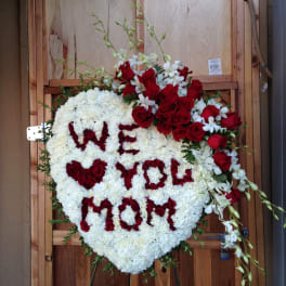 Heart-shaped floral tribute with red roses and white flowers spelling "WE WILL MISS YOU"