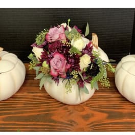 Floral arrangement in a white pumpkin container flanked by two matching pumpkins