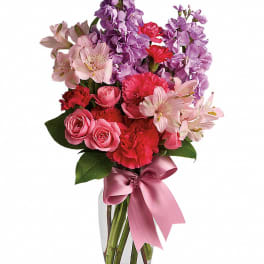 Pink and purple mixed bouquet in a clear glass vase with a satin ribbon