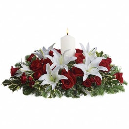 Red roses and white lilies arranged around a lit white candle