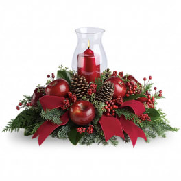 Holiday centerpiece with red apples, pinecones, and a red candle in a glass hurricane