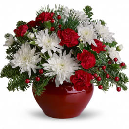 Red and white flowers arranged in a red vase with evergreen accents
