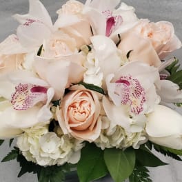 Low arrangement of peach roses, white hydrangeas, and white orchids with pink accents in a glass vase