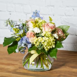 Bouquet of pink roses, blue flowers, and pale green hydrangeas in a glass vase