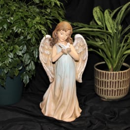 Angel figurine holding a white dove, flanked by two potted plants