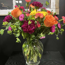 Mixed bouquet of orange roses, magenta carnations, and yellow blooms in a glass vase