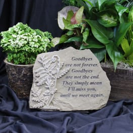 Potted green plants behind a memorial stone with a goodbye message