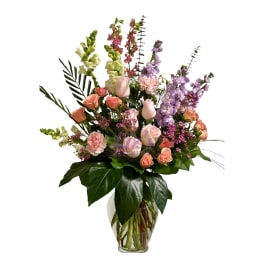Tall mixed arrangement of pink roses, peach spray roses, carnations and lavender stock in a clear glass vase