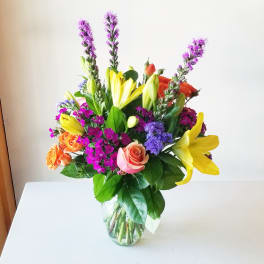 Bouquet of yellow lilies, roses, and purple flowers in a glass vase