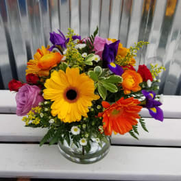 Mixed bouquet of gerbera daisies, roses, and irises in a glass vase