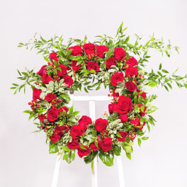 Heart-shaped wreath of red roses and greenery on a white stand