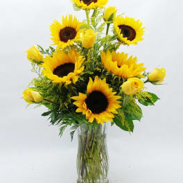 Sunflowers and yellow roses arranged in a clear glass vase