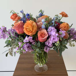 Colorful bouquet of roses, ranunculus, and purple blooms in a glass vase