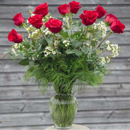 Red roses arranged in a clear glass vase with white filler flowers