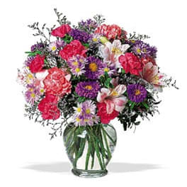 Mixed bouquet of pink, purple, and white flowers in a clear glass vase