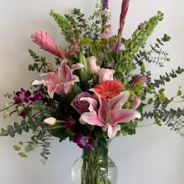 Mixed bouquet of pink lilies, roses, and orchids in a glass vase