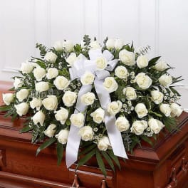 White rose casket spray with a white ribbon on a wooden coffin