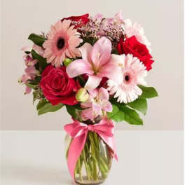 Bouquet of pink and red flowers in a glass vase with a pink ribbon