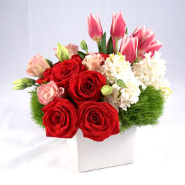 Red roses and pink tulips arranged in a white box with white blooms