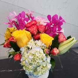 Colorful bouquet with roses, hydrangea, orchids, and lilies in a white vase