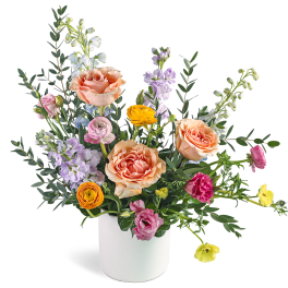 Mixed arrangement of peach roses, ranunculus, and lavender blooms in a white vase