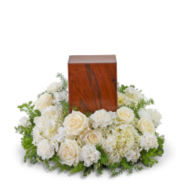 White roses and carnations surround a wooden urn.