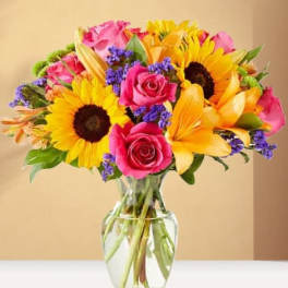 Bouquet of sunflowers, pink roses, and yellow lilies in a glass vase