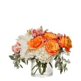 Orange and pink roses with white lilies and hydrangeas in a clear glass vase