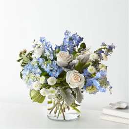 Low blue and white flower arrangement with roses in a clear glass vase