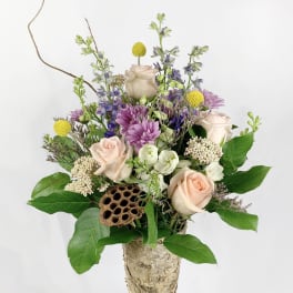 Mixed bouquet in a birch bark vase with pale roses and purple flowers